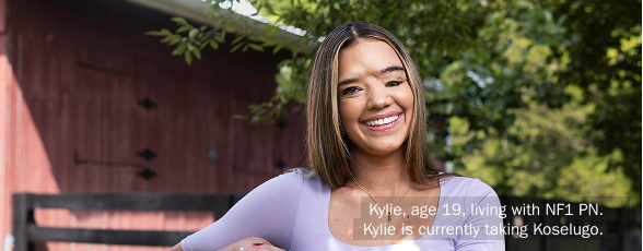 Kylie, age 19, leaning on a fence and smiling at the camera. Kylie takes Koselugo for NF1 PN.